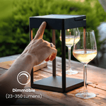 Regolazione manuale di una lampada da esterno dimmerabile su un tavolo con calici da vino.