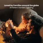 Un uomo e un bambino seduti su un divano, che guardano un oggetto luminoso, con la scritta “Amata dalle famiglie di tutto il mondo: illuminazione d’ambiente per il giardino”.